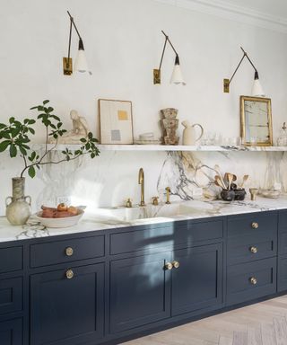 Gold wall lights over a blue kitchen unit with marble countertops.