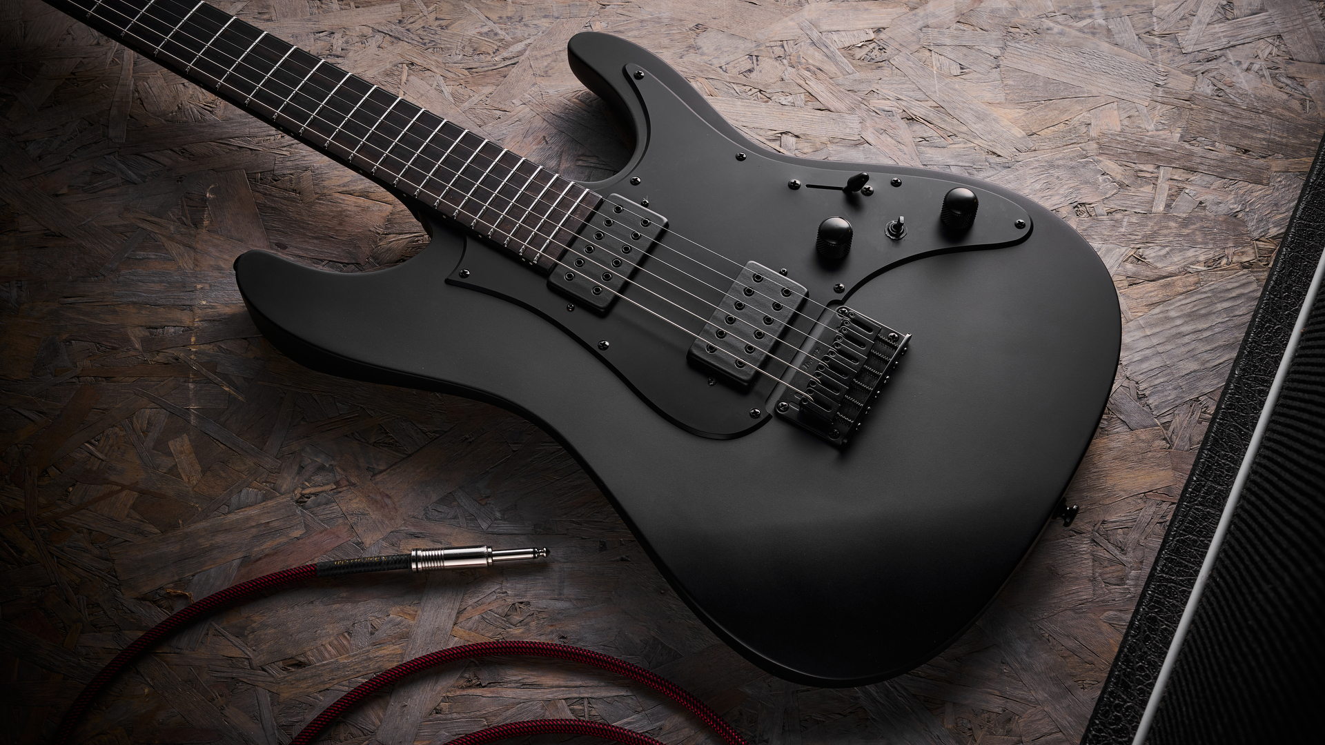 An Ibanez Iron Label AZA41B1 electric guitar lying on a sheet of wood with a guitar cable