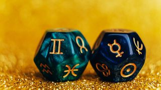Gemini season 2023: Glowing green and blue divination dice Gemini and Mercury on gold colored background with sequins.