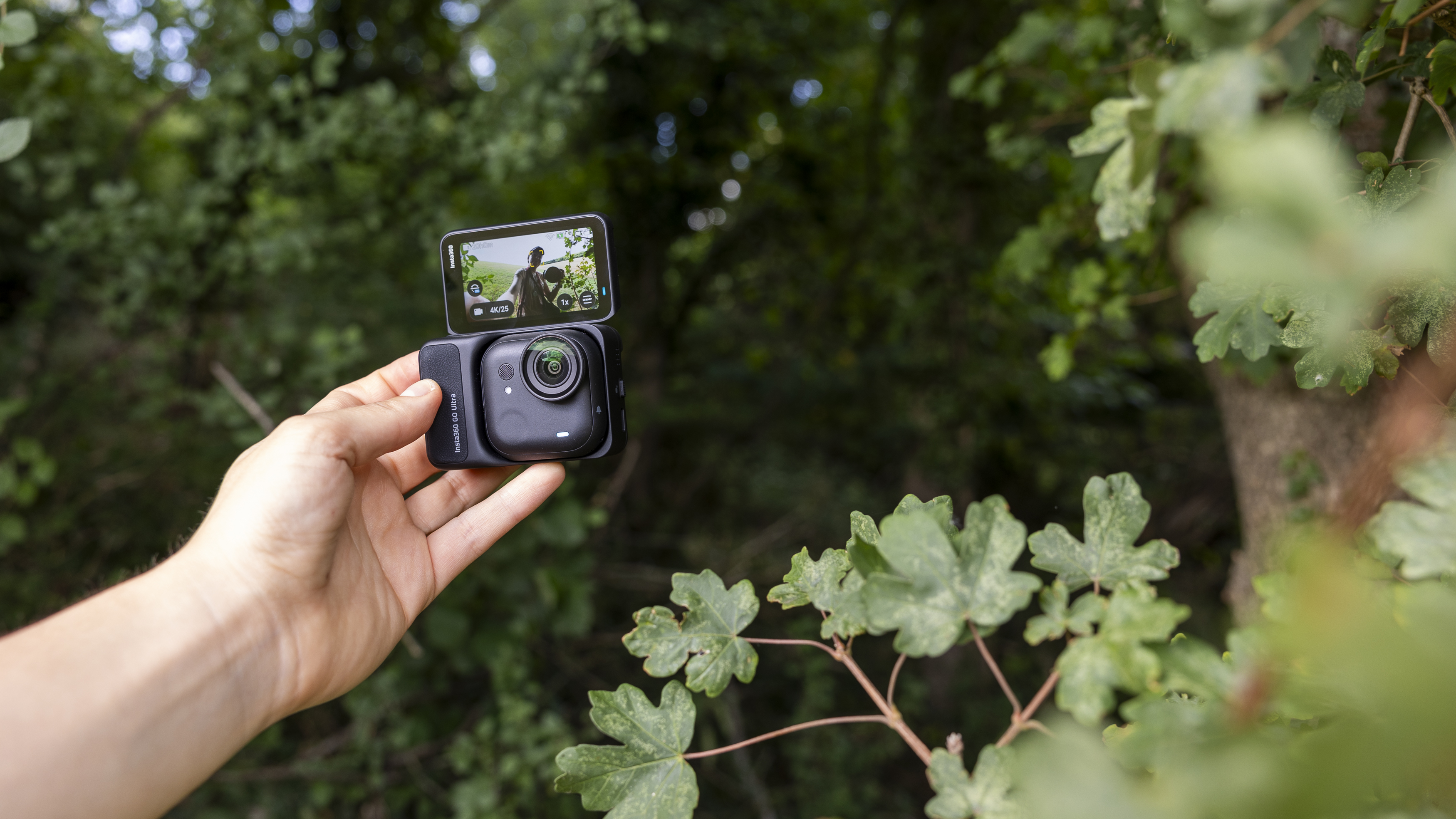 The Insta360 GO Ultra camera held by a female photographer against a green wooded backdrop