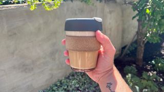 James Frew holding a reusable coffee cup in front of some plants outside in the sun