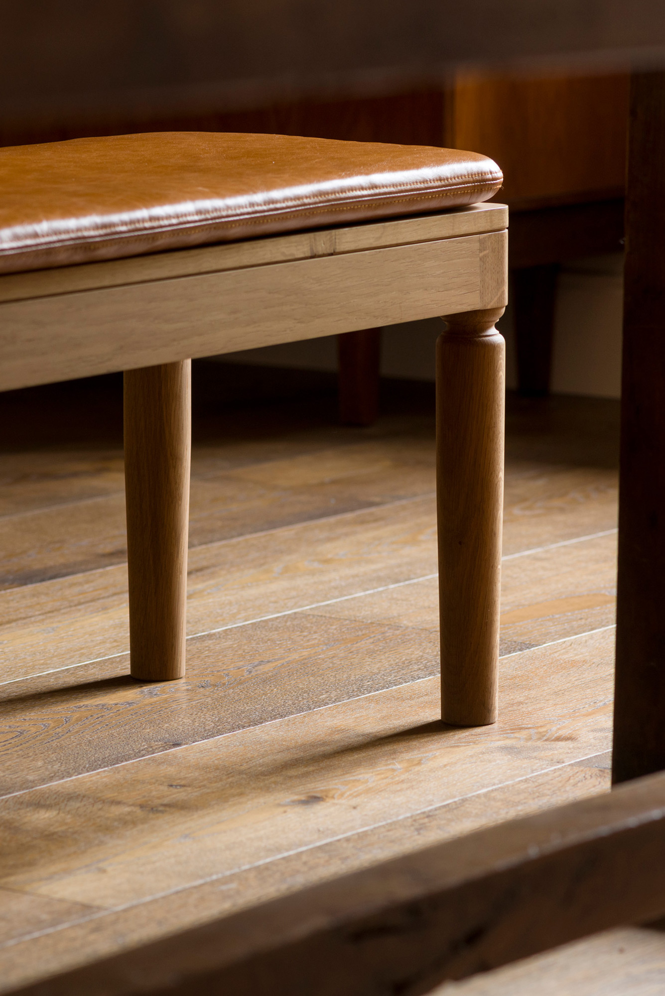 Close-up image of a wooden bench seat with a light brown leather cushion.