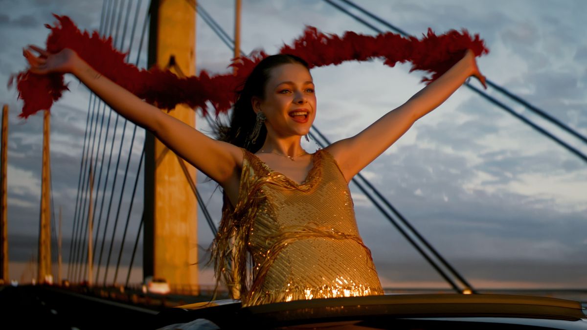 Stella (Alexandra Tyrefors) in a sparkly gold dress and holding a red feather boa out of a sun roof in A Nearly Normal Family episode 1 