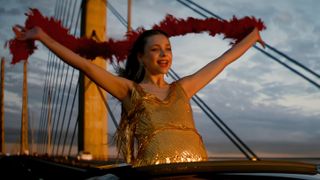 Stella (Alexandra Tyrefors) in a sparkly gold dress and holding a red feather boa out of a sun roof in A Nearly Normal Family episode 1 