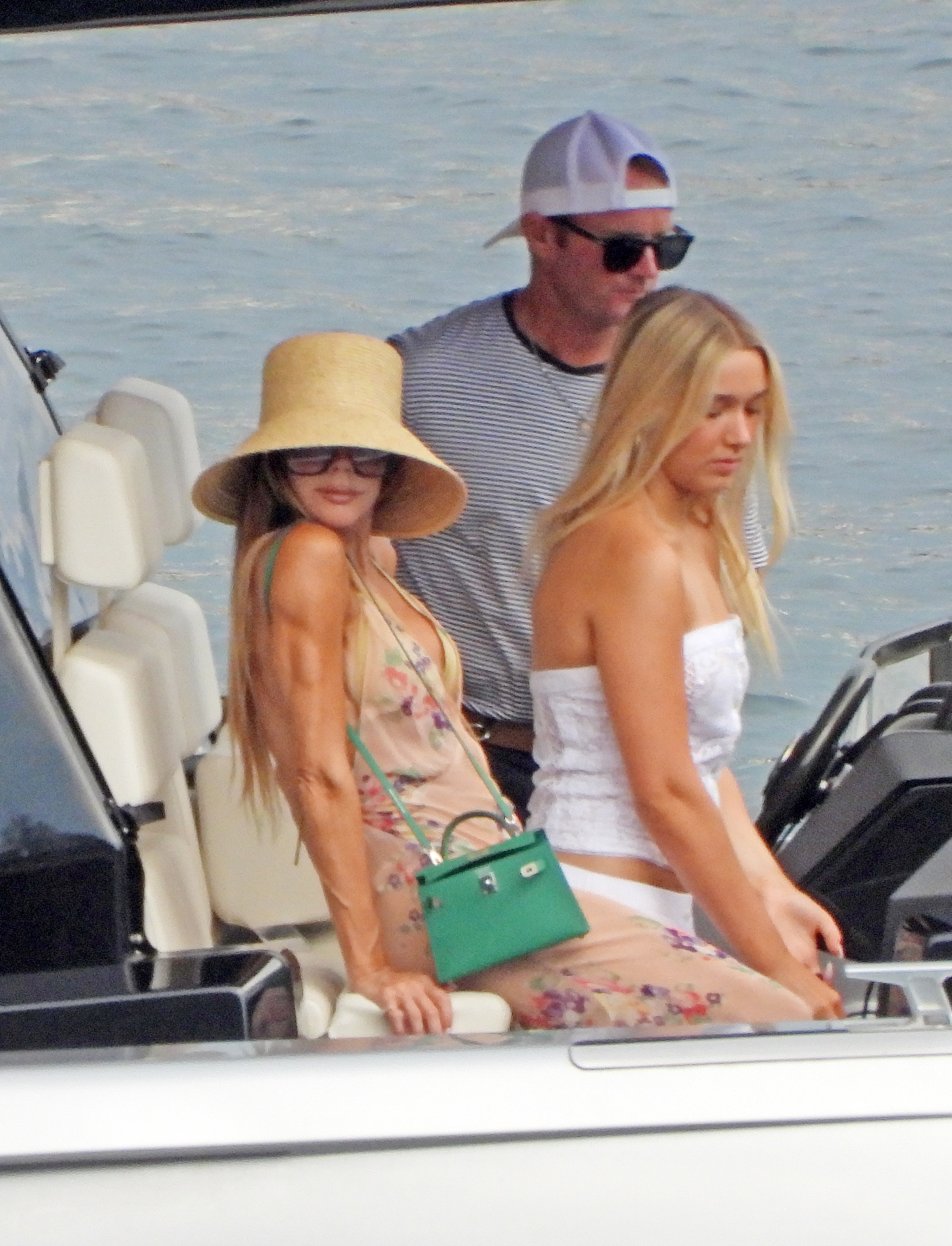 Victoria Beckham wears a sheer naked vacation dress paired with a massive hat and a green Hermes Kelly bag