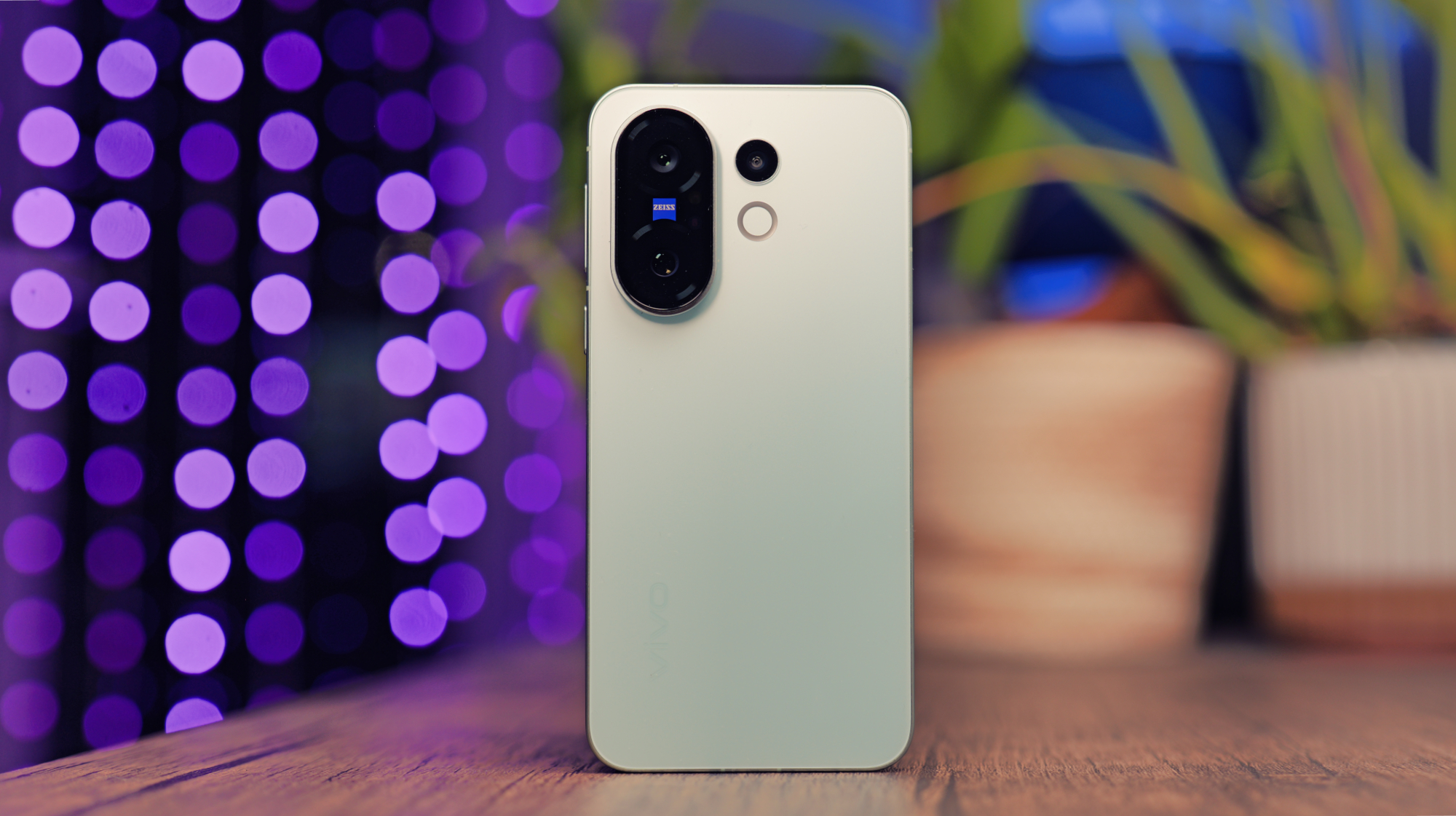 Vivo X200 FE phone on a wooden desk with some lights behind it