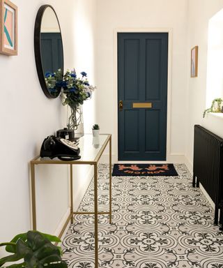 A small entryway with white walls, a blue door, a gold console table, and black and white tiles