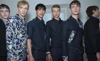 Group of male models wearing dark clothing, standing in a line