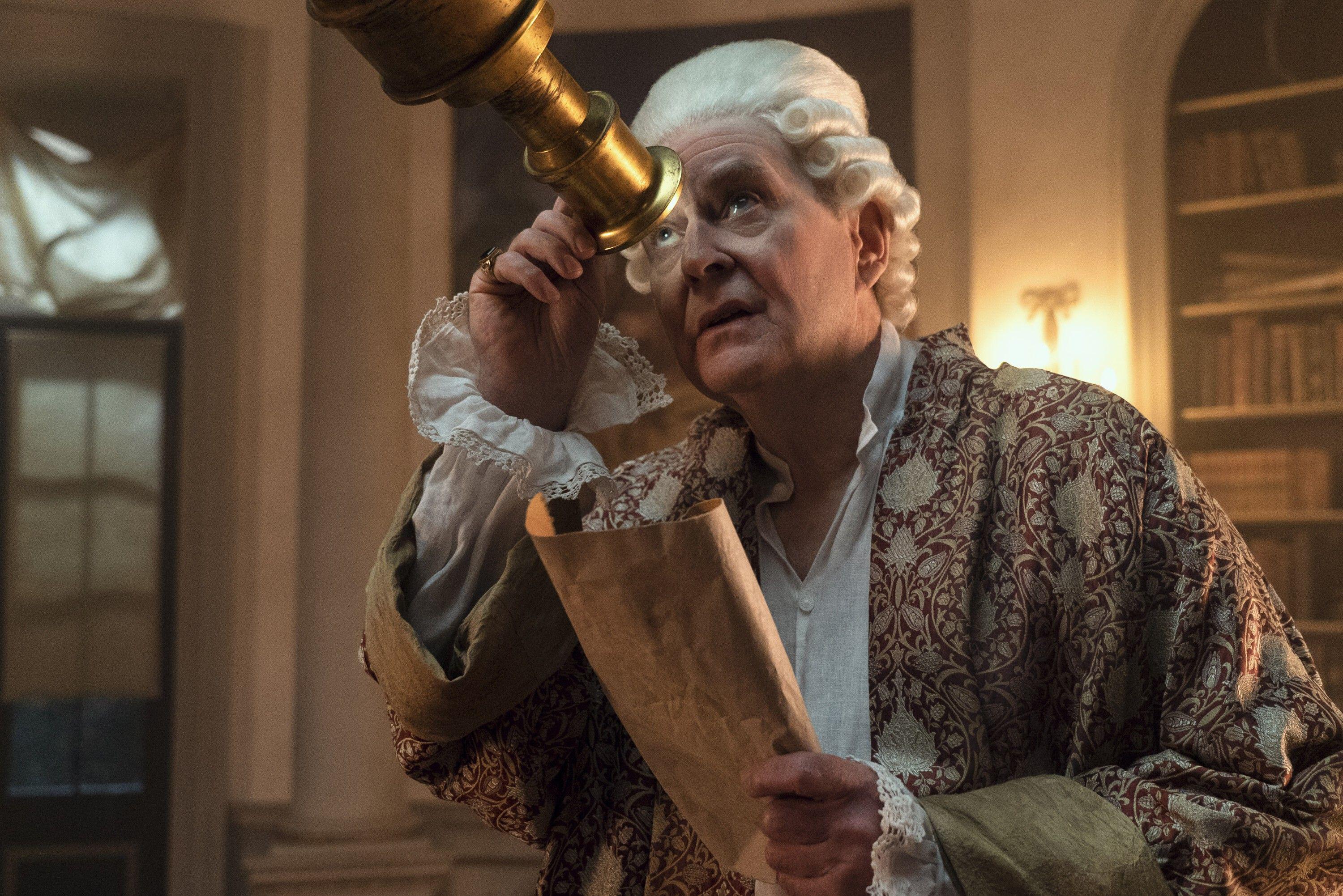 A man in a white wig looks through a telescope in an ornate room