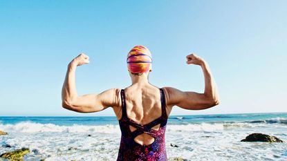 A swimmer flexes her muscles at the beach before plunging into the surf.