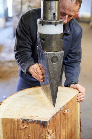 A man preparing to split a large oak log with an industrial axe.