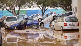 A photo of a flooded street with cars stacked on top of each other from being pushed by water