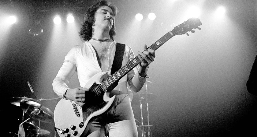 Buck Dharma of Blue Öyster Cult plays his white Gibson SG onstage. He wears all white. The image is black-and-white.