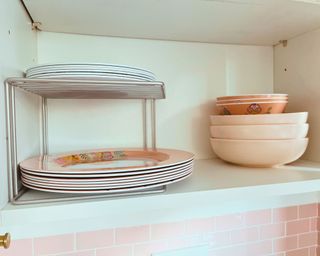 An open kitchen cabinet with a two-tier shelf riser on the left, and stacked pasta and cereal bowls on the right