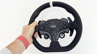 The Moza R3 racing wheel held against a white wall by a reviewer