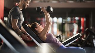 Woman performing a bench press using dumbbells on an incline