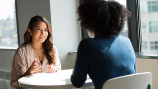 Two people talking over a desk at work.