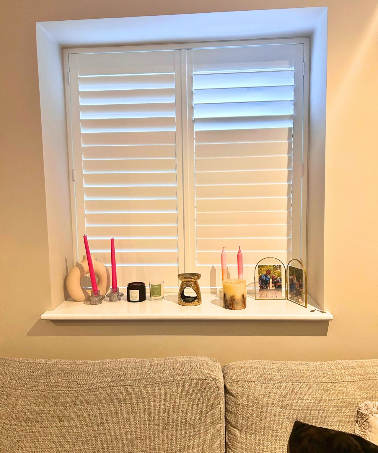 A messy living room shelves with white shutters, candles, oil burner and gold frame