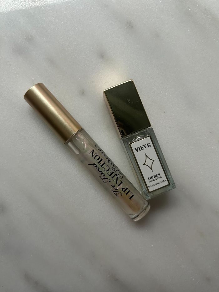 Two of the best clear lip glosses on a marble background
