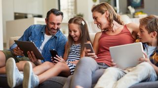 A family sits together on a couch playing games on their phones