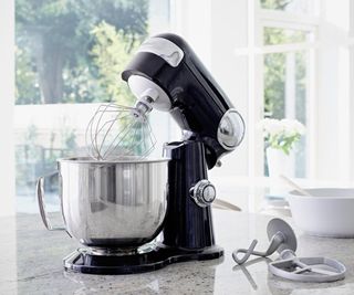 A Cuisinart Precision Stand Mixer in black on a granite countertop next to its attachments