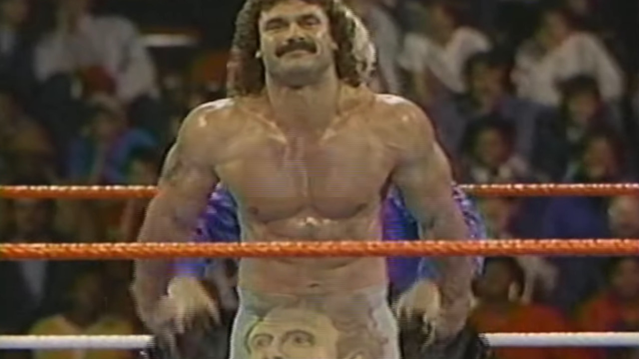 Rick Rude removes his robe to reveal his abs.