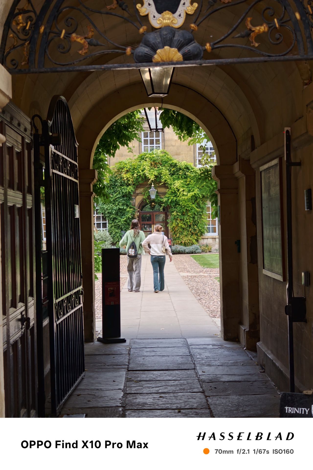 Two people walking through a historic stone archway into a leafy courtyard.