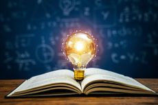 lightbulb placed in an open book with a chalkboard in the background