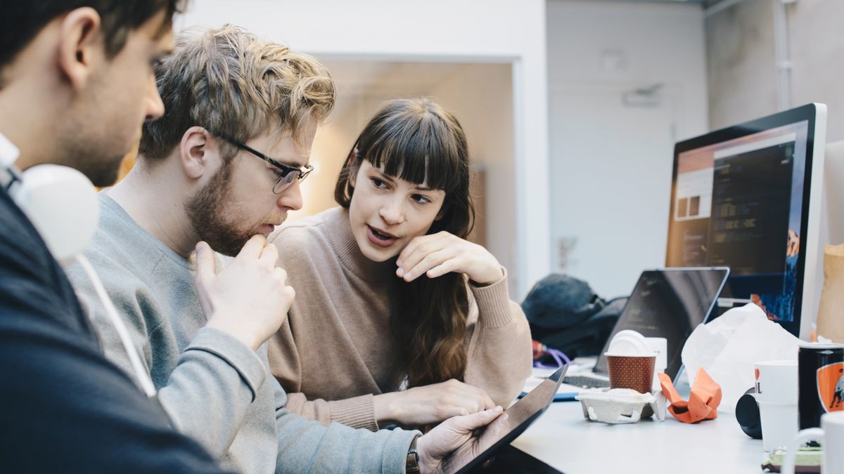 Three colleagues in an IT team sitting around a monitor in an office