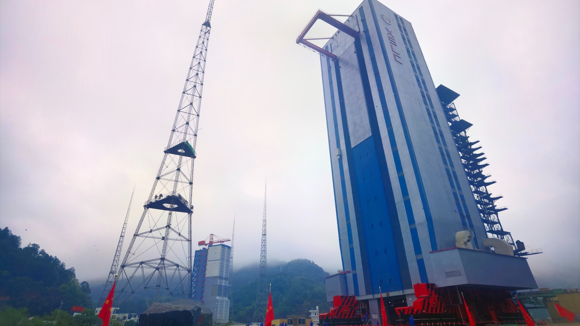 a tall, slender grey building rises up into a grey cloudy sky