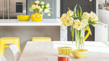 Glass vase filled with yellow flowers on top of kitchen table and countertop