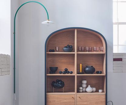A minimalist arched display cabinet decorated with ceramic pots and glassware 