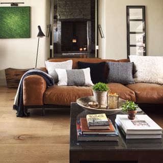 A living room with a brown leather sofa decorated with textured cushions and throw in neutral shades