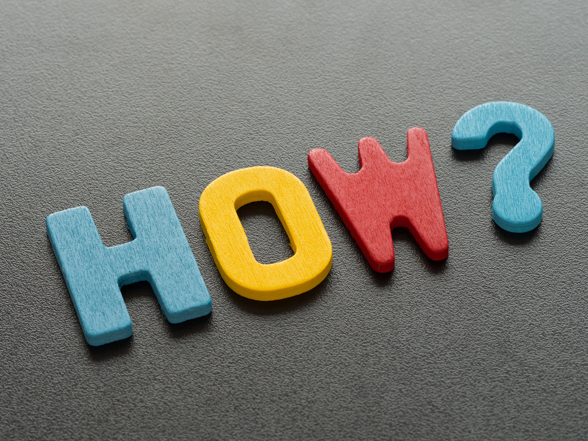 "How" word from wood. Colorful of wooden How question mark on black background.