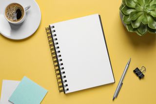 A notepad, pen and coffee on a yellow surface