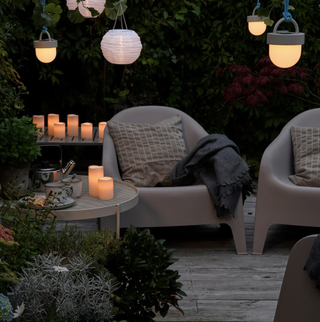 A light-filled patio area with grey decking, grey plastic outdoor armchair and assortment of lanterns and LED candle decor