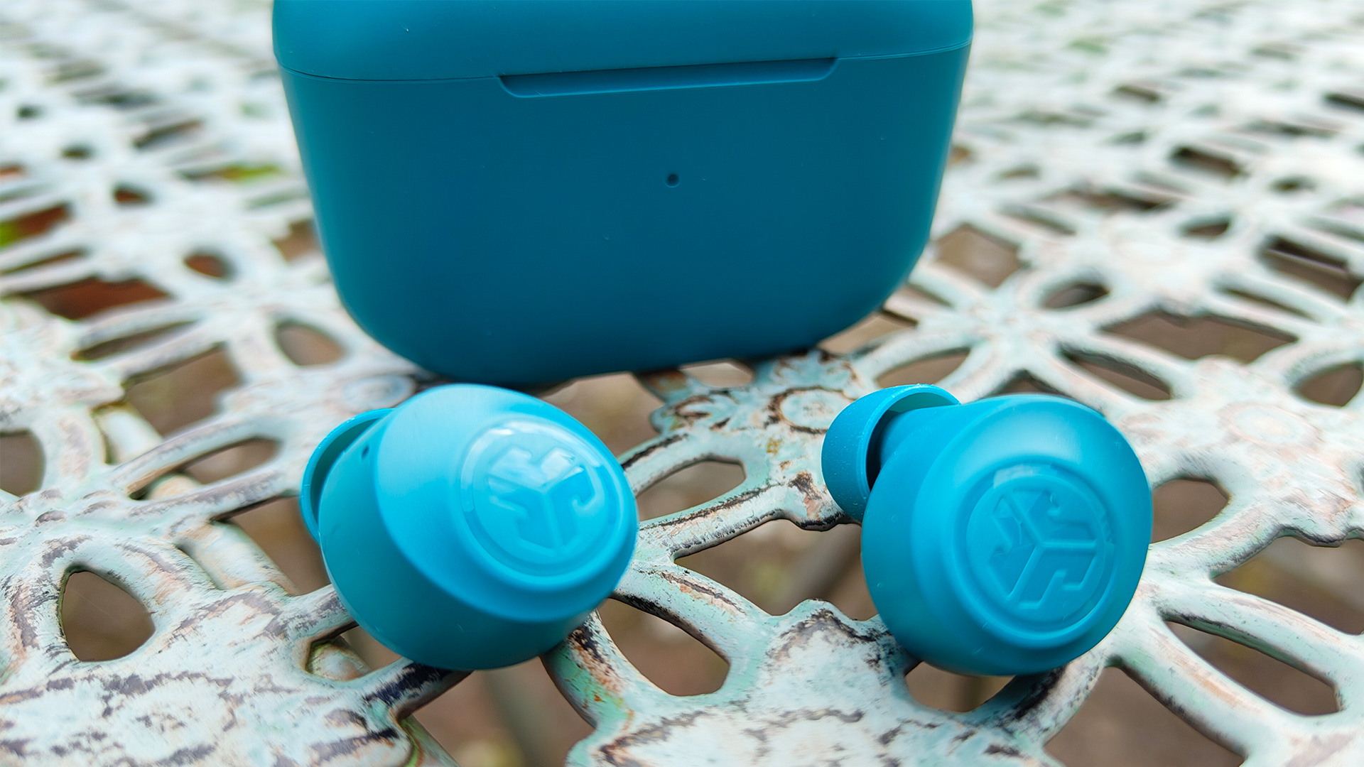 JLab Go Pop+ in-ear headphones on latticed garden furniture next to charging case