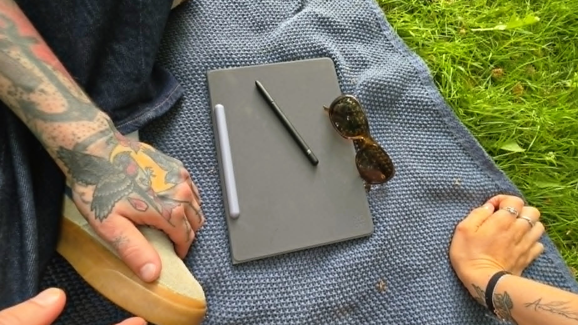 XPPen Magic Note Pad ligger st&amp;auml;ngd p&amp;aring; en filt utomhus, med pennan ovanp&amp;aring; plattan.