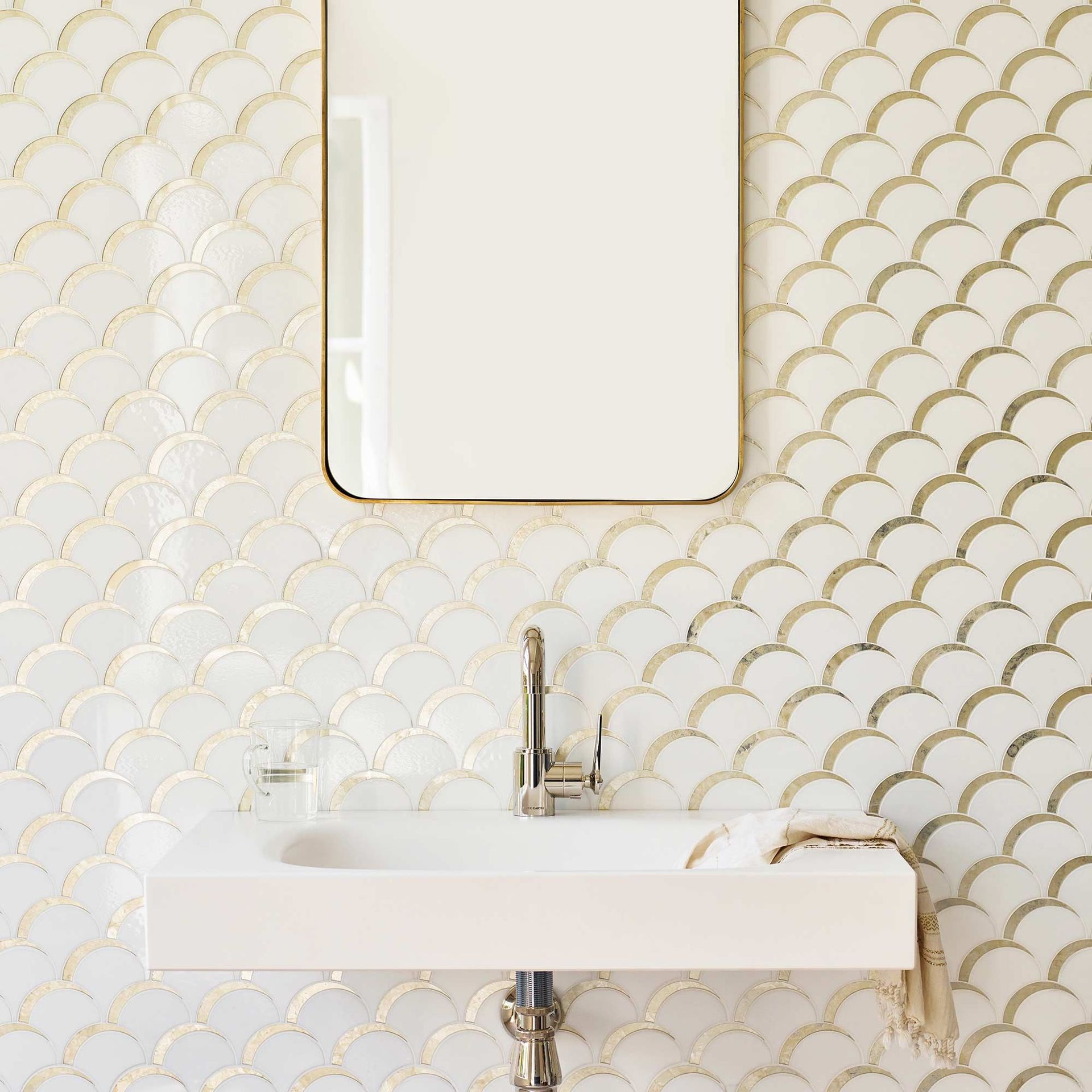 Tile featuring white and gold art deco bathroom tiles behind a white sink and mirror.