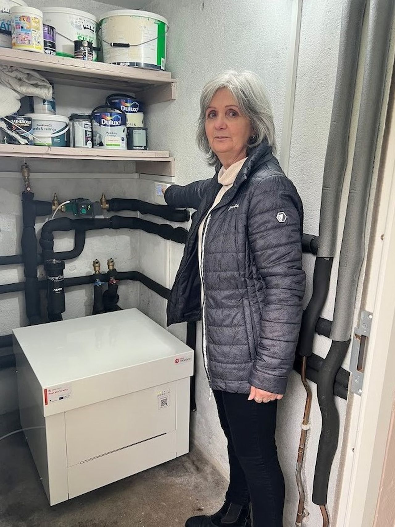 Grandmother stood in front of ground source heat pump in her home
