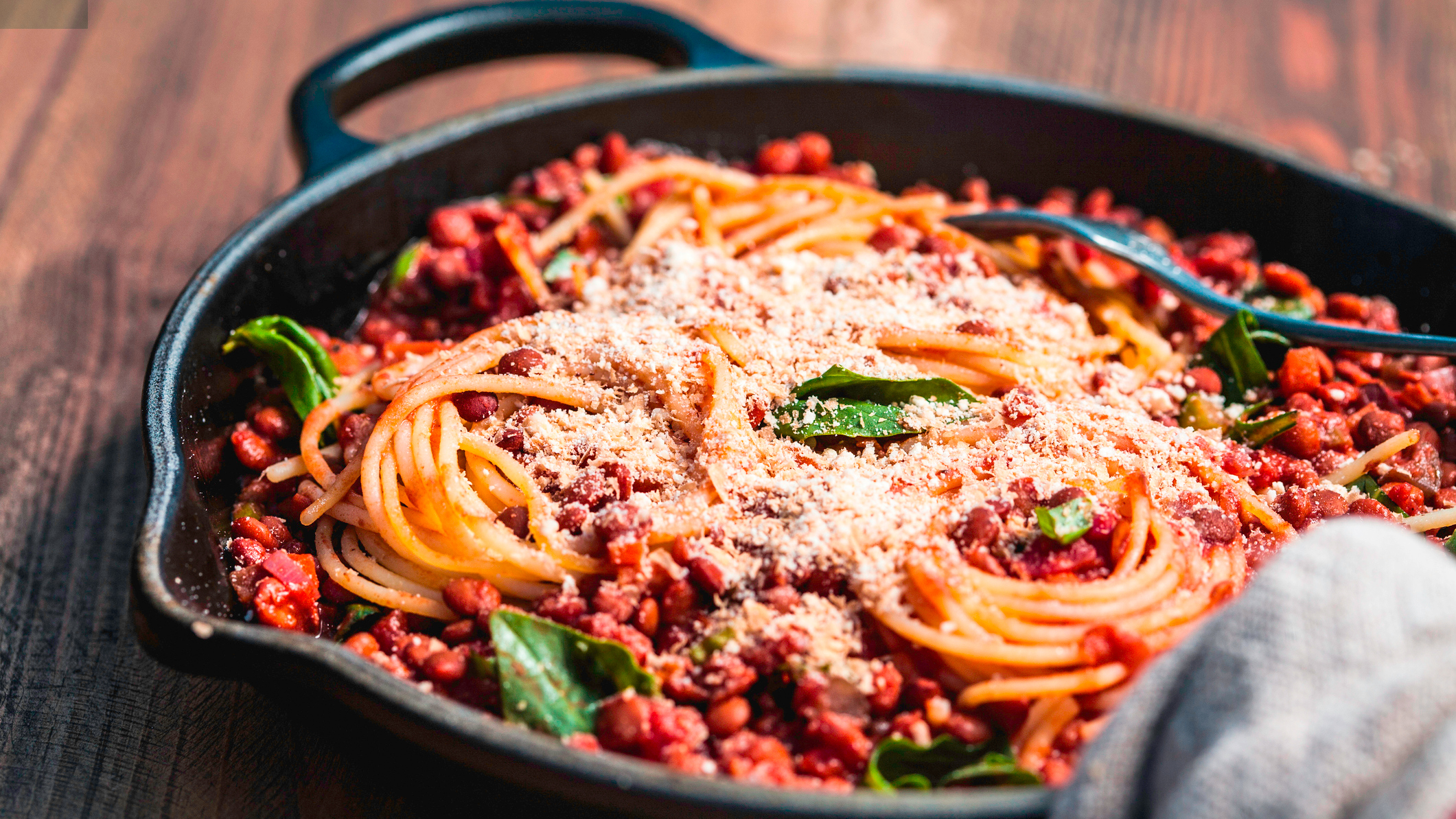 Spaghetti with tomato sauce in skillet on wooden table