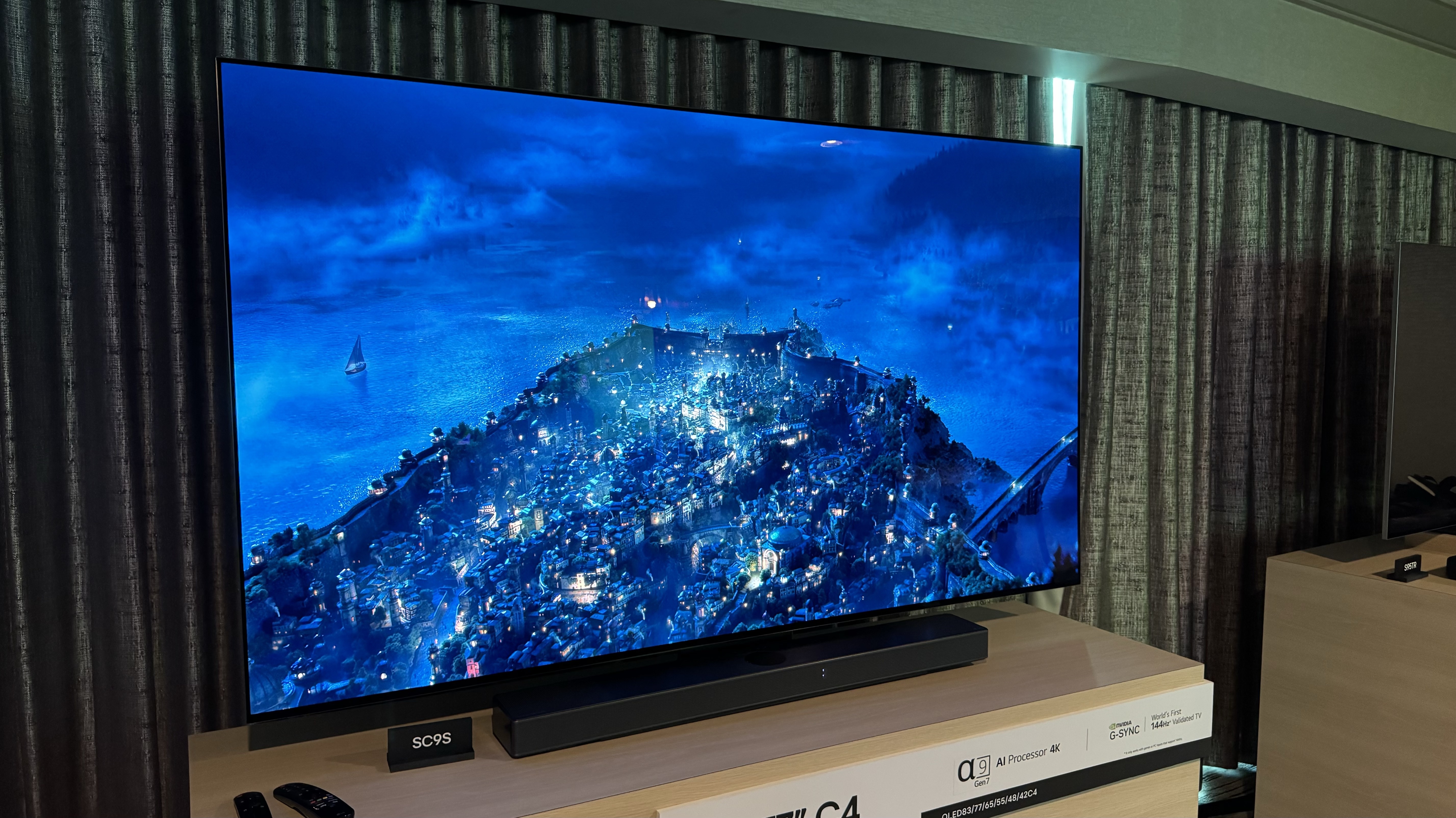 Le téléviseur LG C4 OLED est représenté sur un support devant un rideau gris foncé