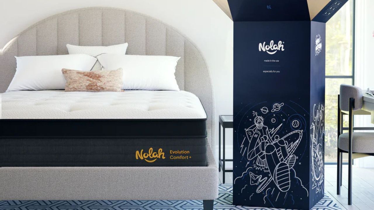 The Nolah Evolution Comfort + Mattress on a gray bed frame. To the bed's right, the mattress's shipping box stands upright.