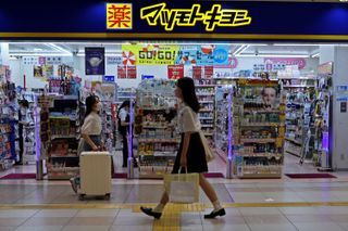 Two women walk in front of the entrance to a drug store in Japan