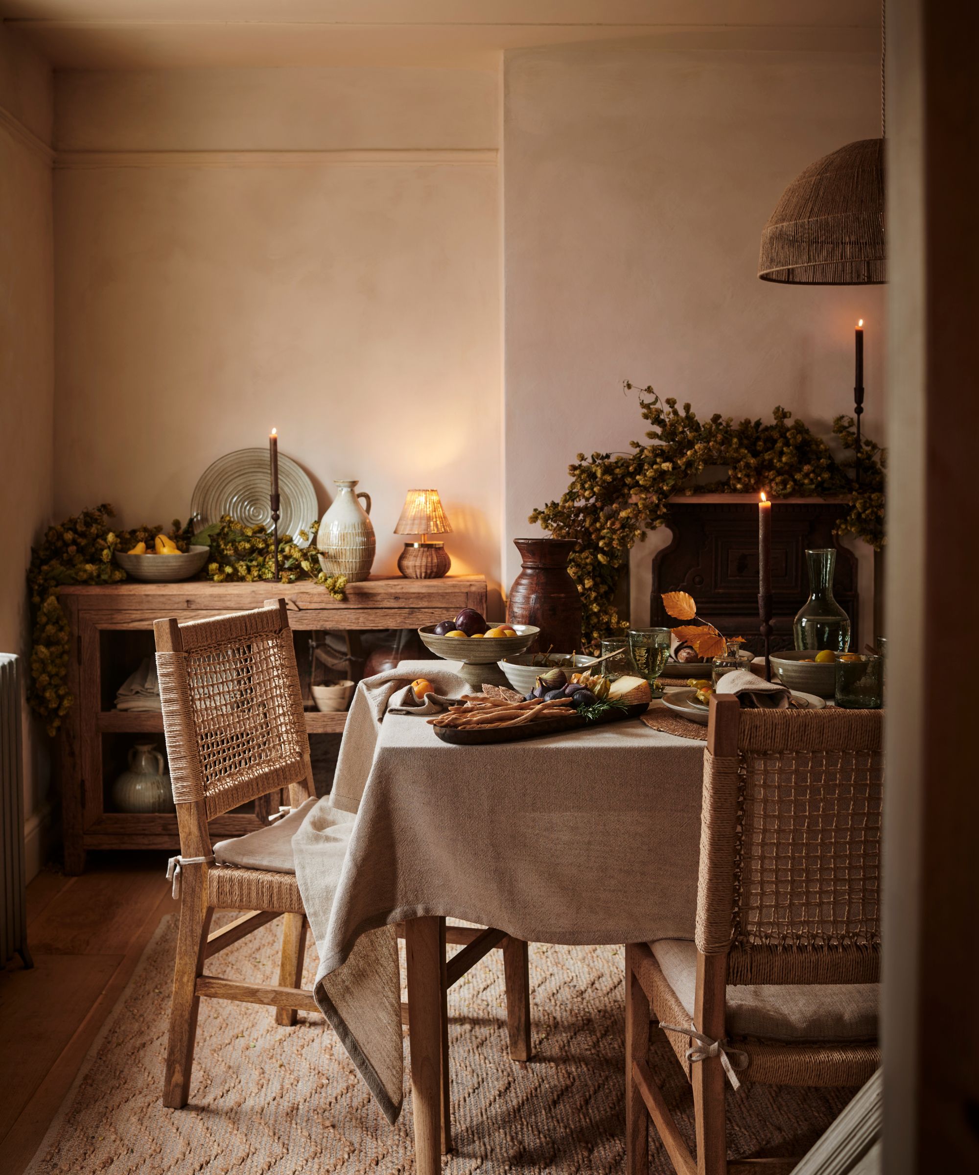 A neutral dining room decorated for fall, with garlands draped over the mantle and sideboard.