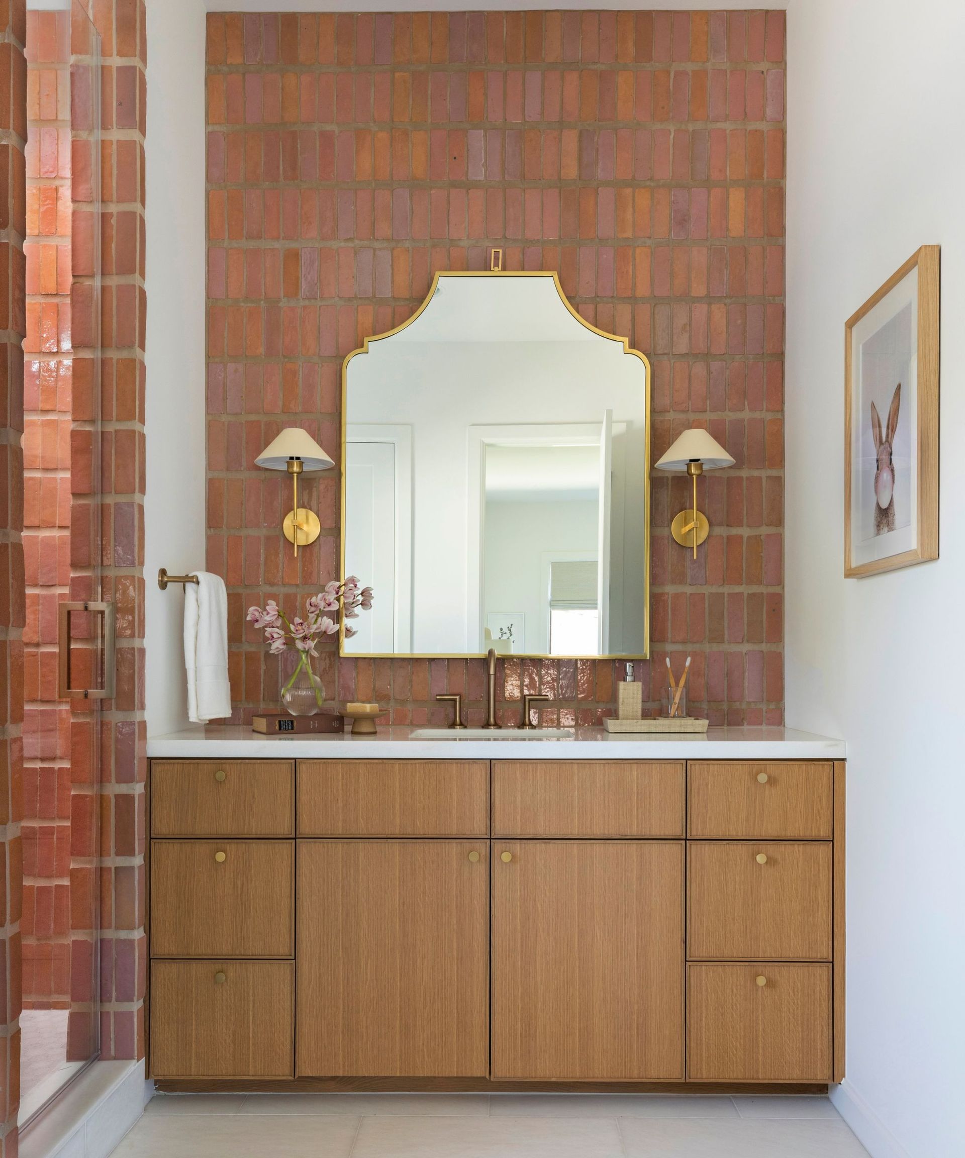 A warm neutral bathroom with terracotta tiles, a wooden vanity, and a gold mirror