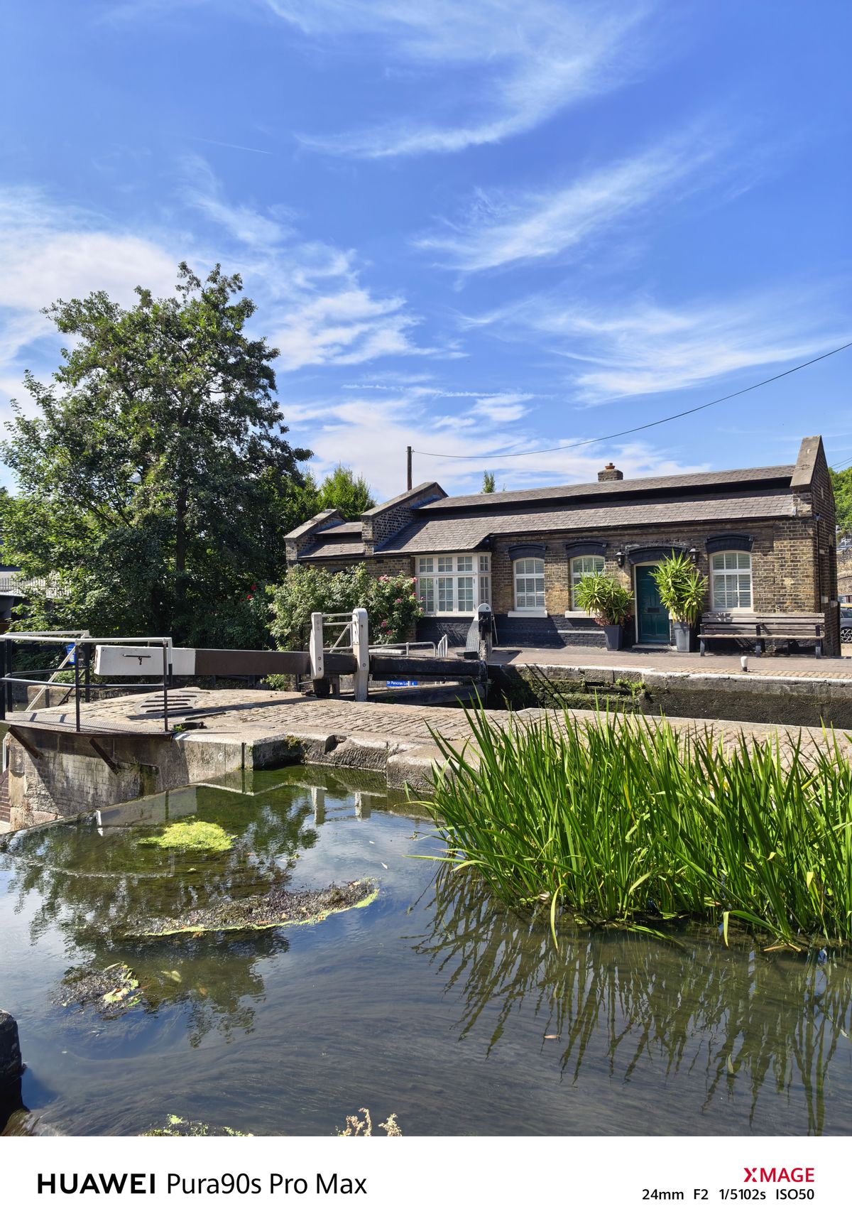 Historic canal-side cottage and lock gates reflected in the water, surrounded by reeds and greenery.