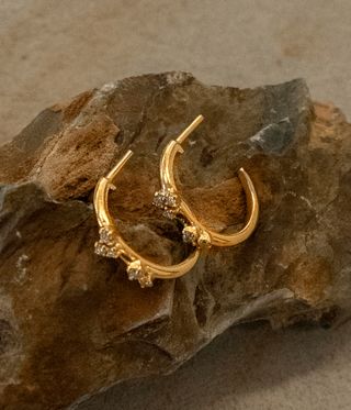 Gold hoop earrings with diamonds resting on a rock