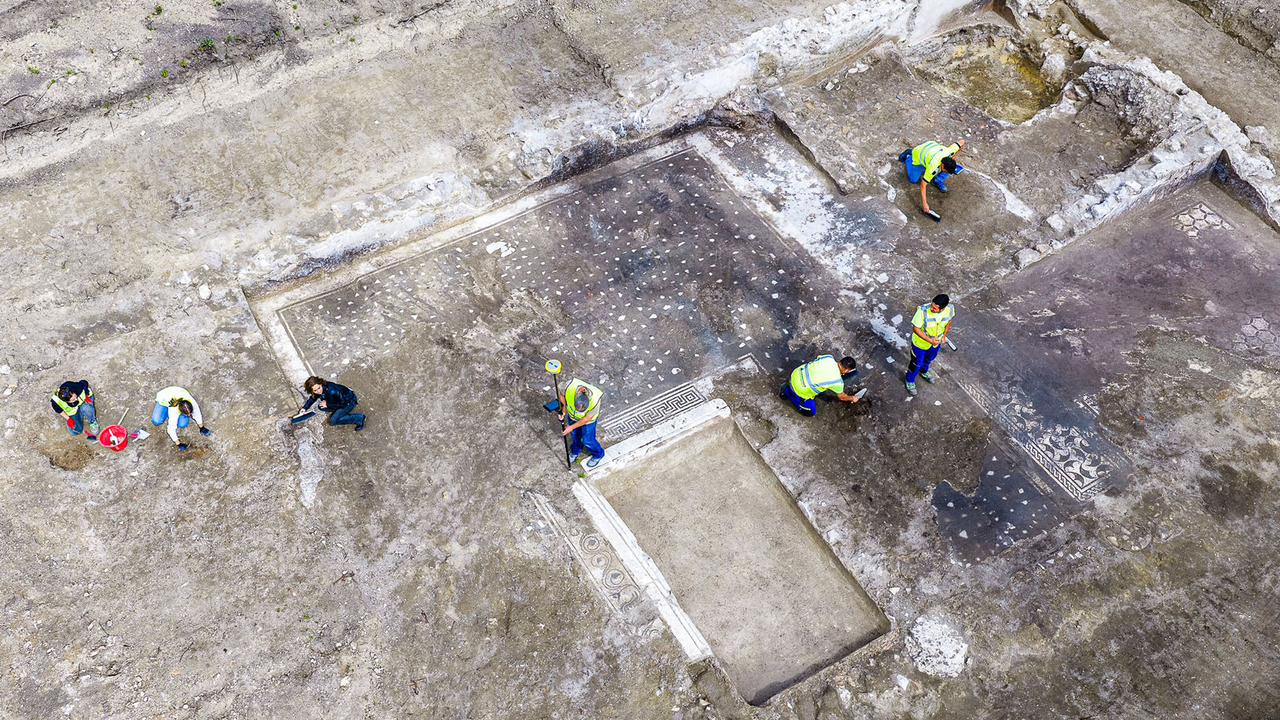 archaeologists work at an ancient Roman site revealing mosaic floors and frescoed walls of a villa