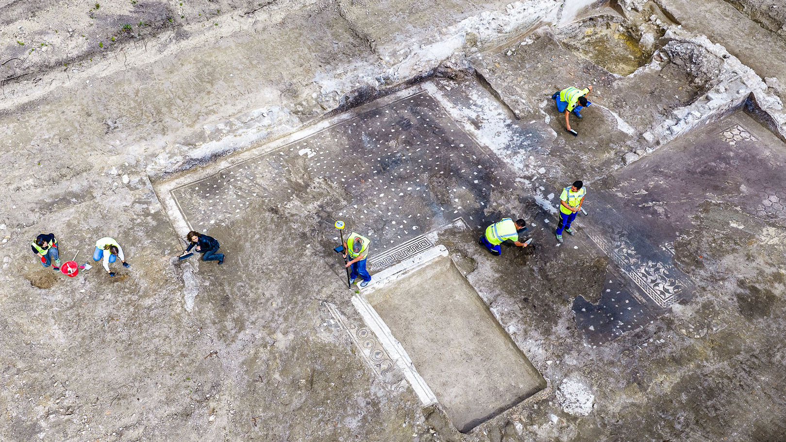 archaeologists work at an ancient Roman site revealing mosaic floors and frescoed walls of a villa